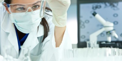 A female medical or scientific researcher or woman doctor looking at a test tube of clear solution in a laboratory with her microscope beside her.